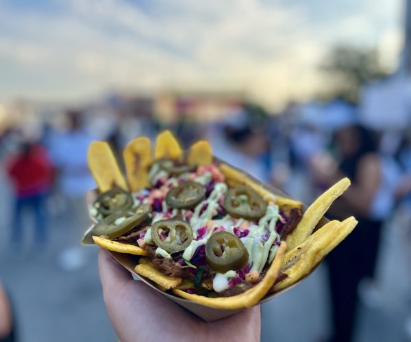 hand holding a plate of nachos with people blurred in the background